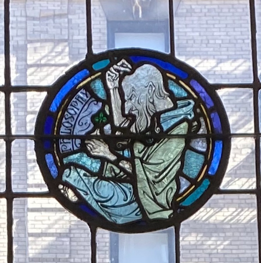 Stained glass art from the window of Grace Dodge Cafeteria depicting a figure scratching his head and holding a plant