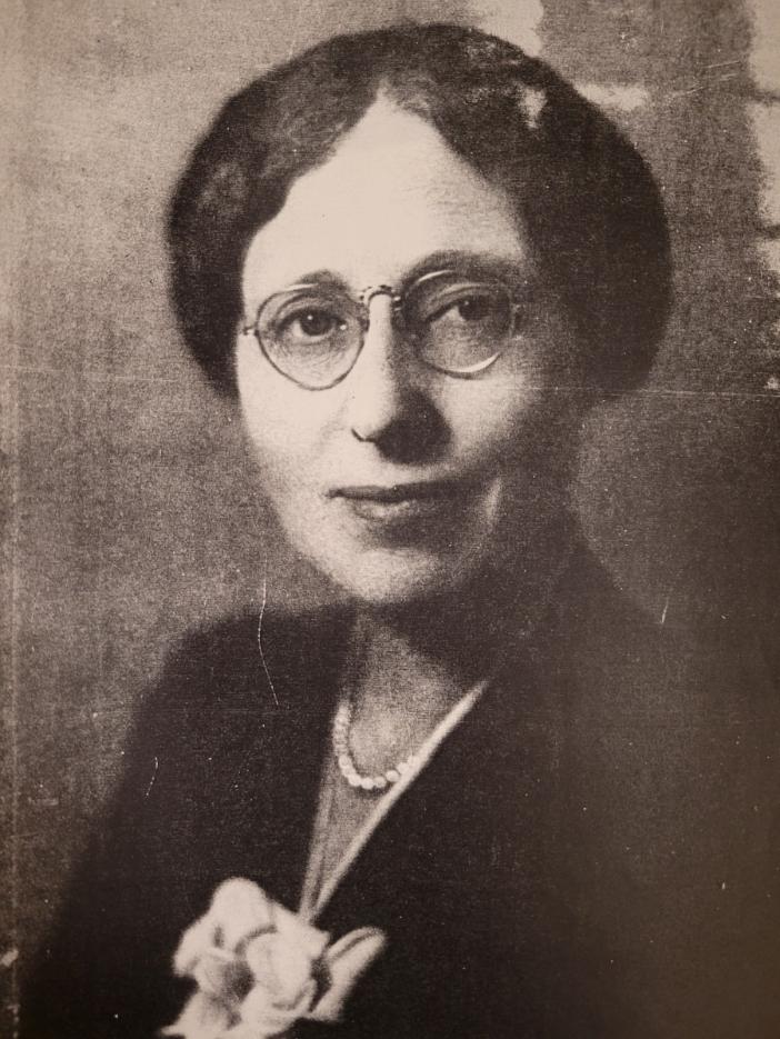 Black and white photograph of Professor Mabel Carney. She faces the camera, wearing round glasses and dark clothes. Her eyes are clear and bright and stare into the camera. She wears a soft smile and a pearl necklace. Her hair is sculpted to frame her face and parted in the middle.