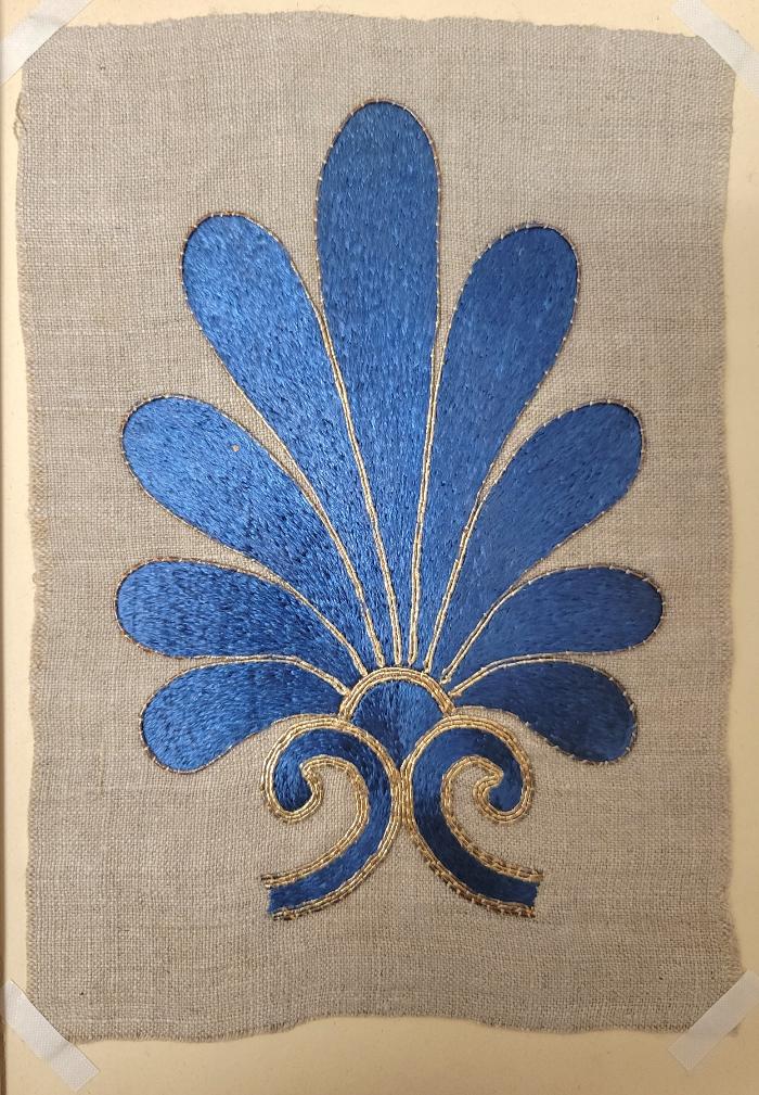Embroidery example featuring a blue floral or palmette design with gold border and embellishments. The design is embroidered on linen.