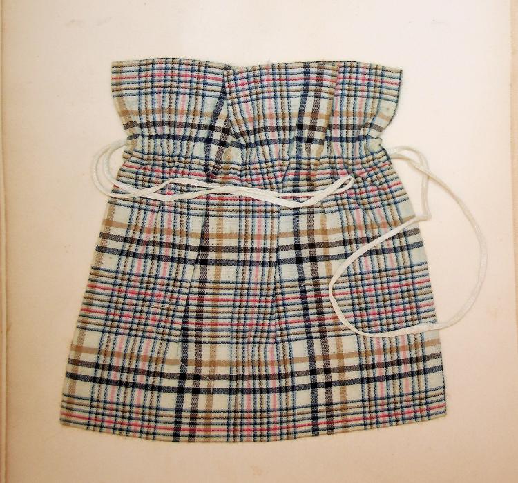 Example of model 13, small drawstring bag, from Woolman’s Sewing Course. The bag is plaid, with alternating black, tan, and red stripes over a cream fabric.